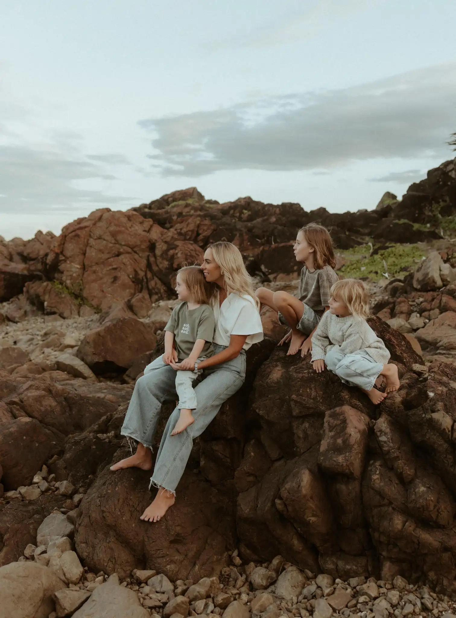 Ali sitting on coastal rocks at dusk with her three children, looking out to sea